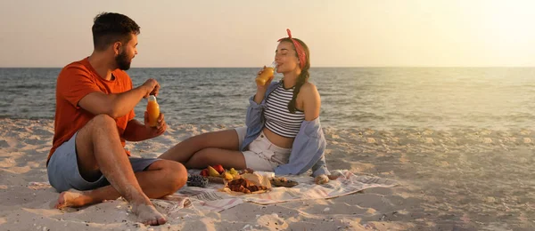 Lovely couple having picnic on sandy beach near sea, space for text. Banner design