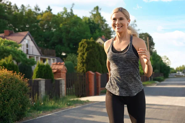 近所をワイヤレスイヤホンでジョギングしている女性 — ストック写真