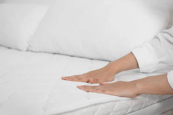 Woman touching soft white mattress on bed, closeup