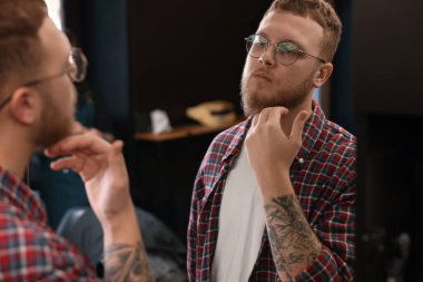 Berber dükkanında aynanın yanındaki sakallı genç adam.