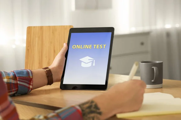 Man taking online test on tablet at desk indoors, closeup