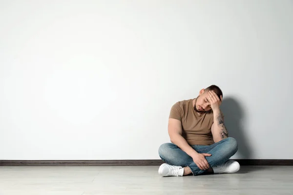 白い壁の近くの床に座っている悲しい若い男屋内 テキストのためのスペース — ストック写真