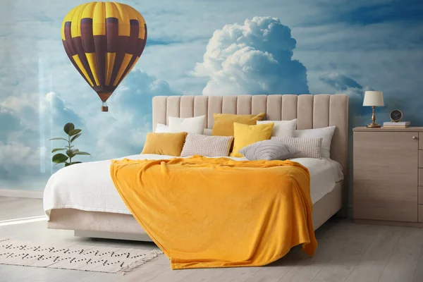 Beautiful wallpaper with image of hot air balloon in cloudy sky over misty sea in bedroom interior