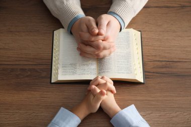 Oğlan ve vaftiz ebeveyni ahşap masada birlikte dua ediyor, yakın plan.