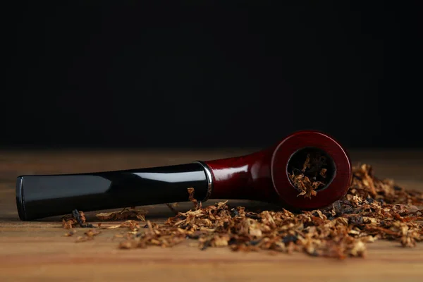 Smoking pipe and dry tobacco on wooden table against dark background. Space for text