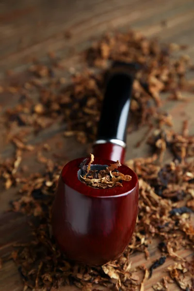 Smoking pipe and dry tobacco on wooden table, closeup