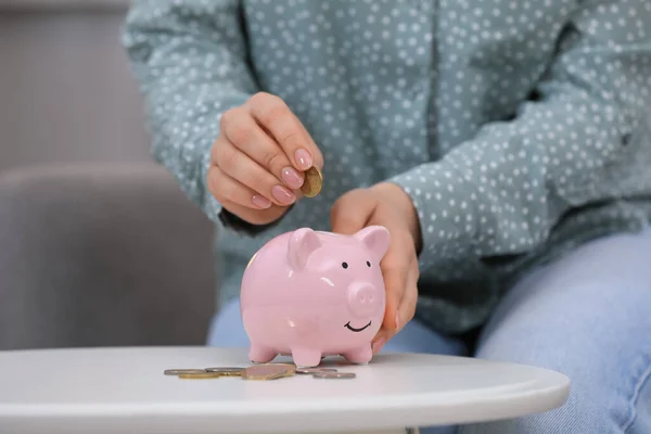 Young Woman Putting Coin Piggy Bank Table Indoors Closeup — стоковое фото