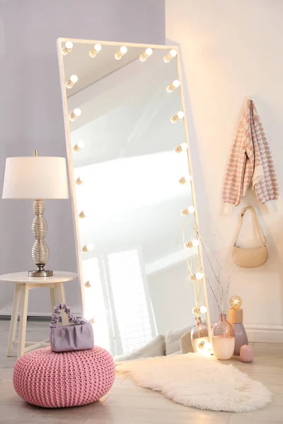 Large mirror with light bulbs and knitted pouf in stylish room. Interior design