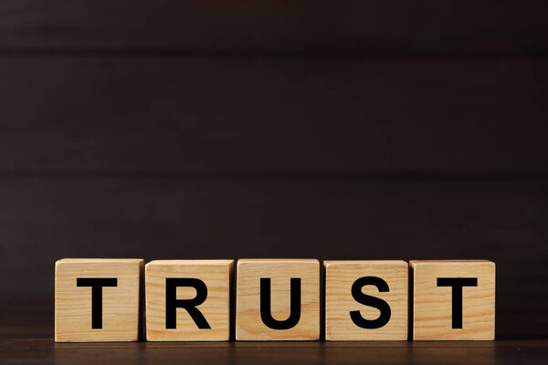 Cubes with word TRUST on wooden table. Space for text