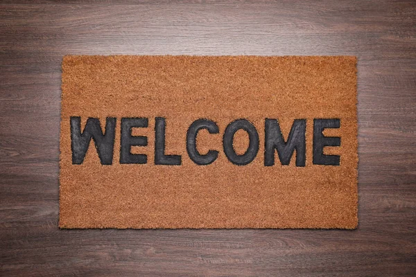 Stylish door mat with word Welcome on wooden floor, top view