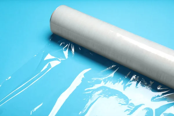 Roll of transparent stretch wrap on turquoise background, closeup