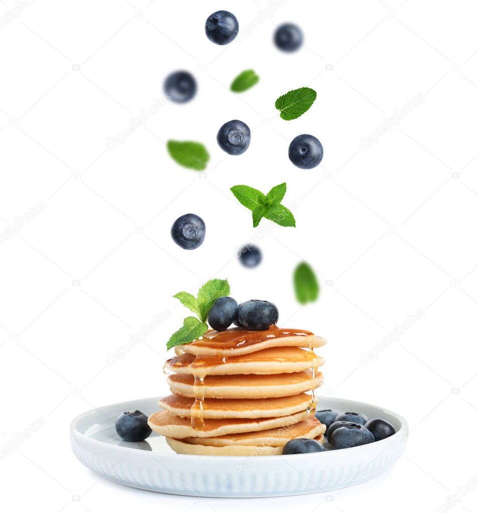 Fresh blueberries and mint leaves falling onto stacked pancakes against white background