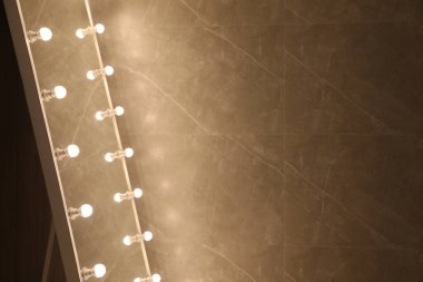 Kahverengi duvarın yanında ampulleri olan modern ayna, yakın plan. Metin için boşluk