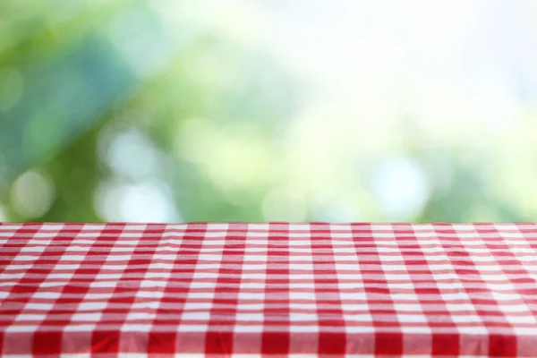 Table with checkered picnic cloth outdoors on sunny day. Space for design