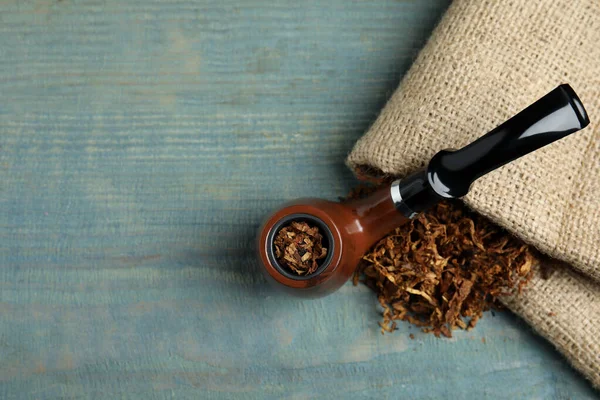 Smoking pipe, dry tobacco and sackcloth on blue wooden table, top view. Space for text