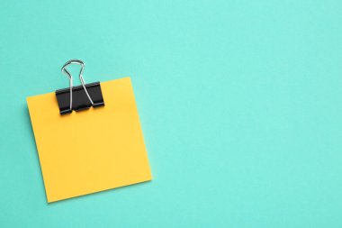 Turkuaz arka planda siyah kağıt kıskacı olan boş turuncu bir not, üst manzara. Metin için boşluk