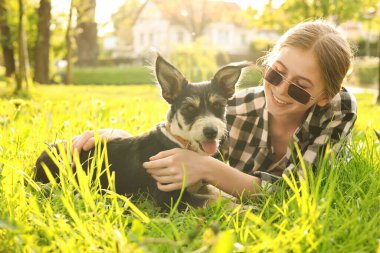 Parktaki yeşil çimlerde dinlenen sevimli köpeğiyle genç bir kız.