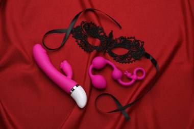 Kırmızı kumaşta pembe seks oyuncakları ve siyah dantel maske.