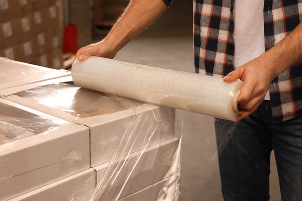 Worker wrapping boxes in stretch film at warehouse, closeup