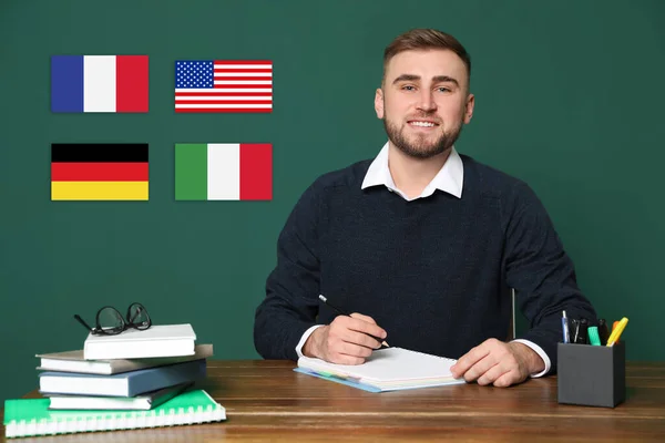 Portrait of foreign languages teacher at wooden table and different flags green chalkboard