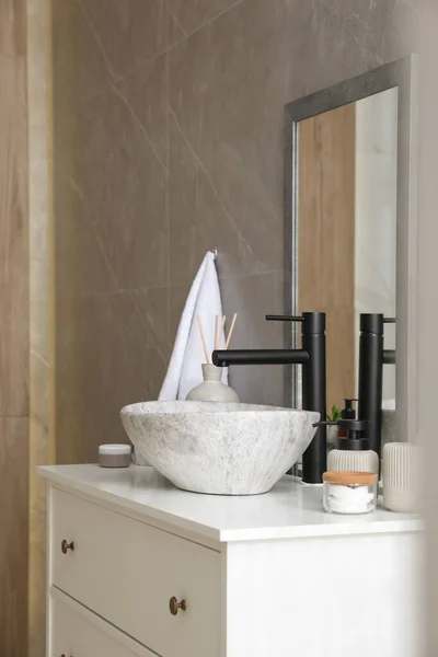 Stone vessel sink with faucet and toiletries on white countertop in bathroom