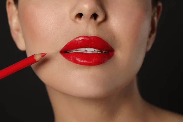 Young woman with beautiful red lip pencil on black background, closeup