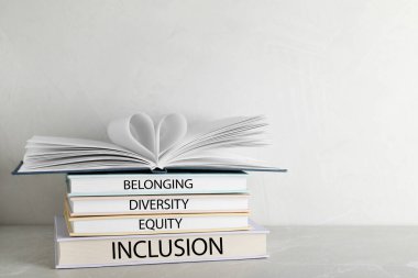 Beyaz arkaplana karşı tablonun üzerinde sözcükler, çeşitlilik, eşitlik, katkı içeren ciltli kitap yığını