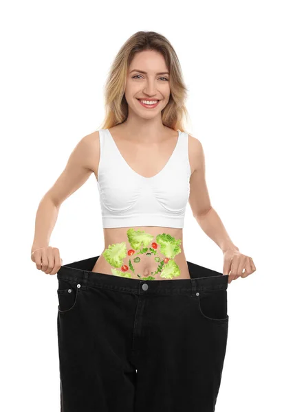特大のジーンズを着たスリムな若い女性と白い背景を背景に彼女の腹に野菜のイメージ 健康的な食事 — ストック写真
