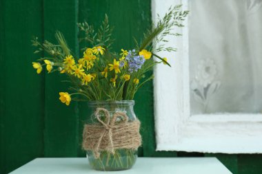 Pencerenin yanındaki masada cam vazoda duran güzel kır çiçekleri.