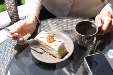 Kahve içen ve dışarıda cam masada lezzetli tatlılar yiyen bir kadın.