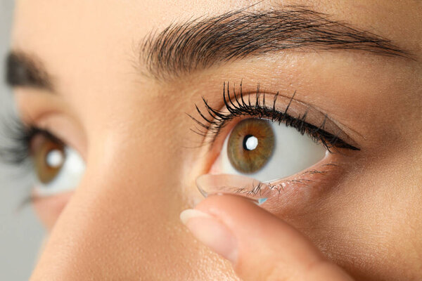 Young woman putting contact lens in her eye, closeup