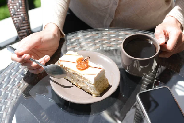 Kahve içen ve dışarıda cam masada lezzetli tatlılar yiyen bir kadın.