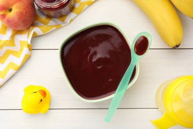 Lezzetli, püre bebek maması ve beyaz ahşap masa üzerindeki malzemelerle dolu bir kase.