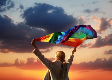 Gün batımında gökyüzünde parlak LGBT bayrağı taşıyan kadın