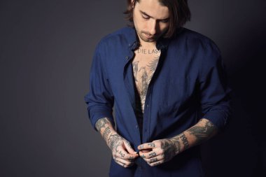 Siyah arka planda dövmeleri olan genç bir adam.