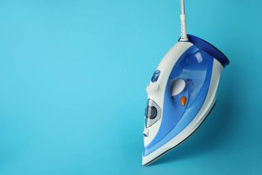 Açık mavi arka planda modern bir ütü, metin için boşluk. Ev aletleri