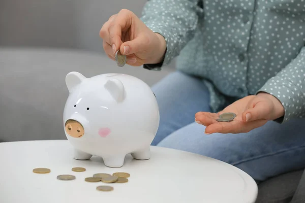 Young Woman Putting Coin Piggy Bank Table Indoors Closeup — Stok fotoğraf