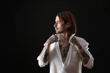 Siyah arka planda dövmeleri olan genç bir adam.