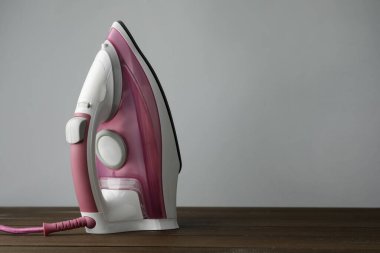 Açık gri arka plana karşı ahşap masa üzerinde modern bir ütü, yazı için yer. Ev aletleri