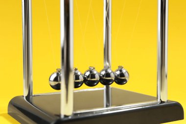 Newton's cradle on yellow background, closeup. Physics law of energy conservation