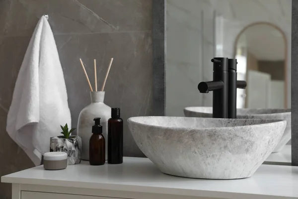 Stone vessel sink with faucet and toiletries on white countertop in bathroom