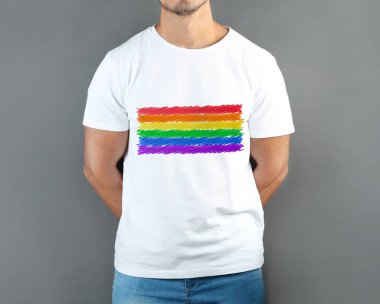 Gri arkaplanda LGBT gurur bayrağı resmi olan beyaz tişört giyen genç adam