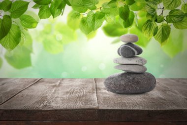 Yeşil yaprakların altında, ahşap masaya istiflenmiş taşlar, bulanık arka plana karşı, yazı için yer. Zen kavramı