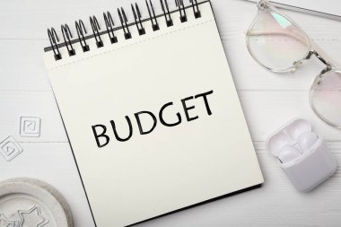 Sözcük bütçeli defter, gözlükler ve kulaklıklar beyaz ahşap masada, düz yatıyordu.