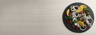 Dilimlenmiş tuzlu ringa filetosu, maydanoz, kırmızı biber, soğan halkaları ve limonlu açık bej ahşap masa, üst manzaralı metin. Pankart tasarımı