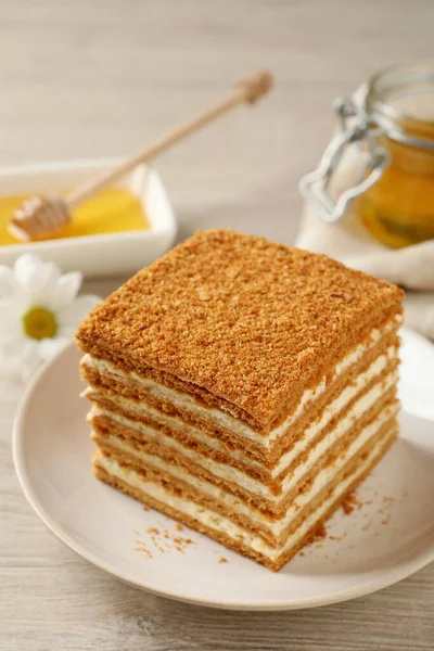 Slice of delicious layered honey cake served on wooden table, closeup