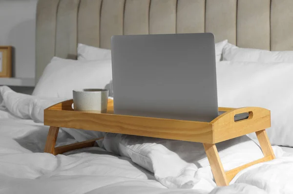 現代のノートパソコンとベッドの上の芳香族ドリンクのカップと木製のトレイ室内 — ストック写真