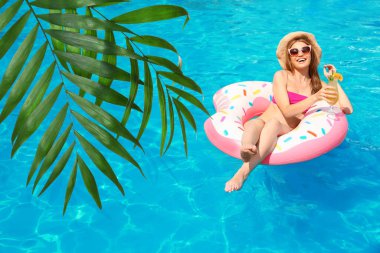 Güzel yeşil tropikal yapraklar ve güneşli bir günde bilardoda kokteyl içen genç bir kadın.