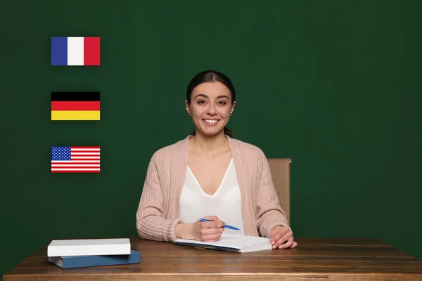 Portrait of foreign languages teacher at wooden table and different flags green chalkboard