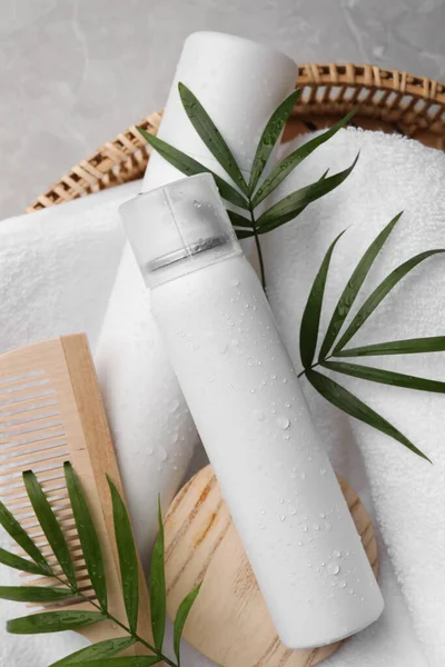 Dry shampoo sprays, towel and wooden comb with green leaves in wicker basket on table, top view